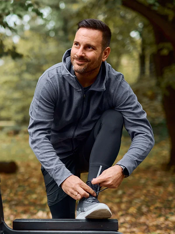 smiling man wearing running gear and tying shoes on park bench